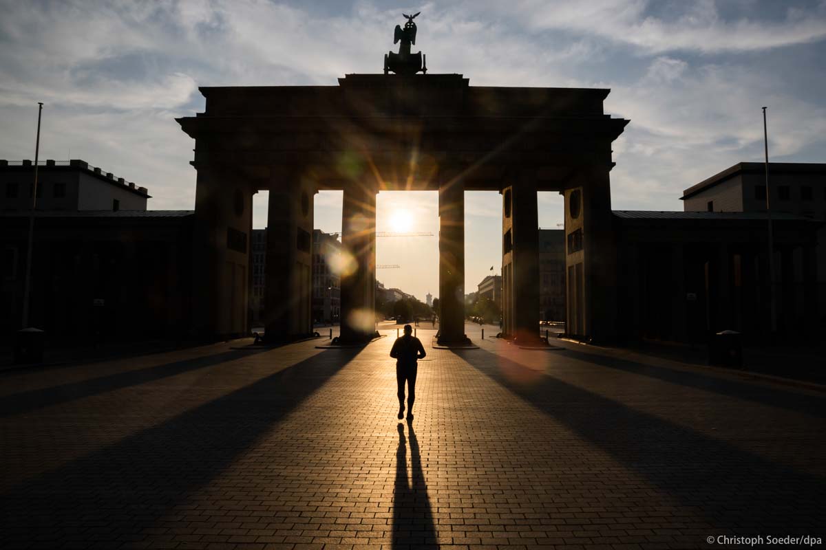 A man walks through the Brandenburg Gate at sunrise.